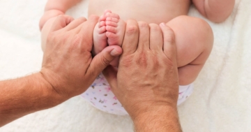 Piedi di neonato tenuti tra le mani di un genitore