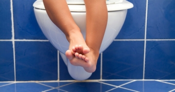 Gambe di bambino seduto sul water per stitichezza