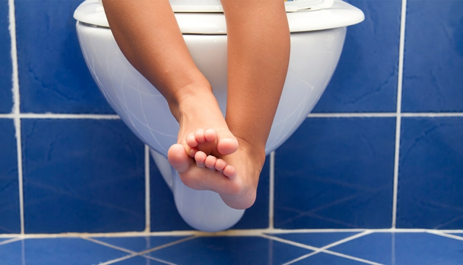 Gambe di bambino seduto sul water per stitichezza