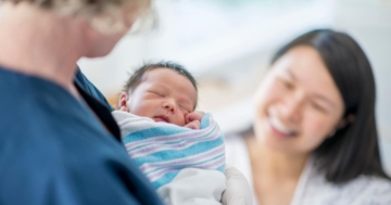 Una neomamma guarda sorridendo il bambino in braccio all'ostetrica