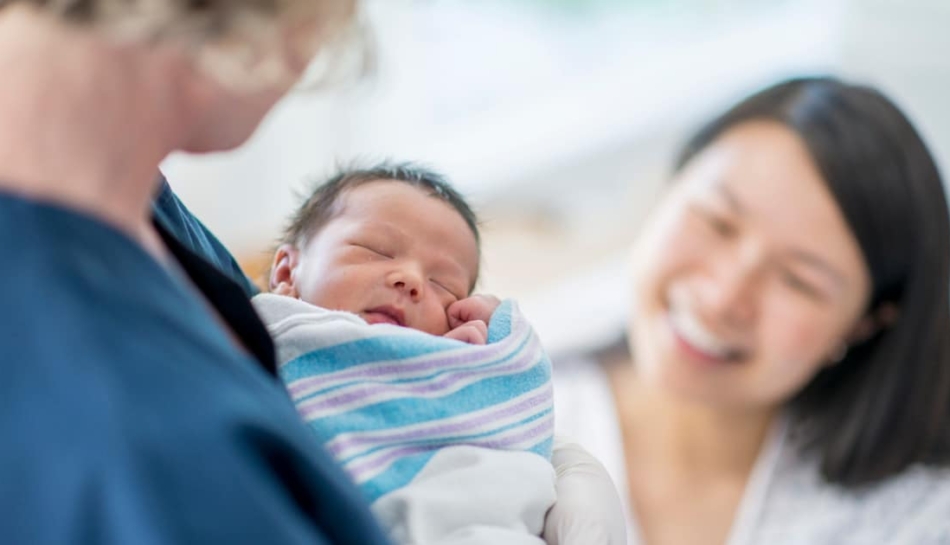 Una neomamma guarda sorridendo il bambino in braccio all'ostetrica