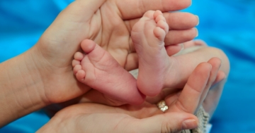 Piedi di neonato tenuto tra le mani della mamma