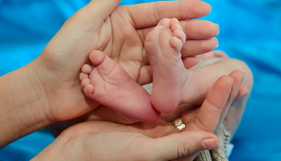 Piedi di neonato tenuto tra le mani della mamma