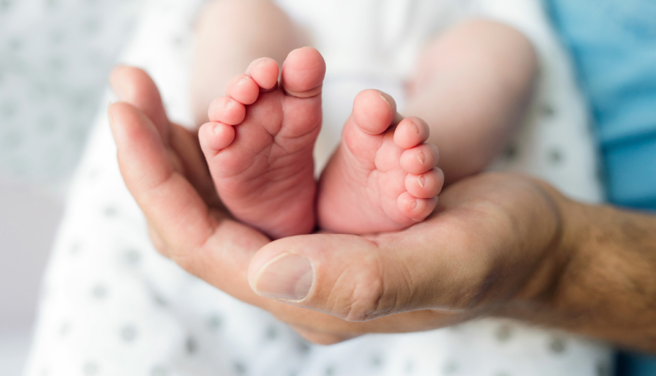 Mano di un papà che tiene i piedini del figlio appena nato