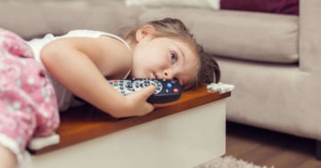 Little girl lying on sofa holding remote control