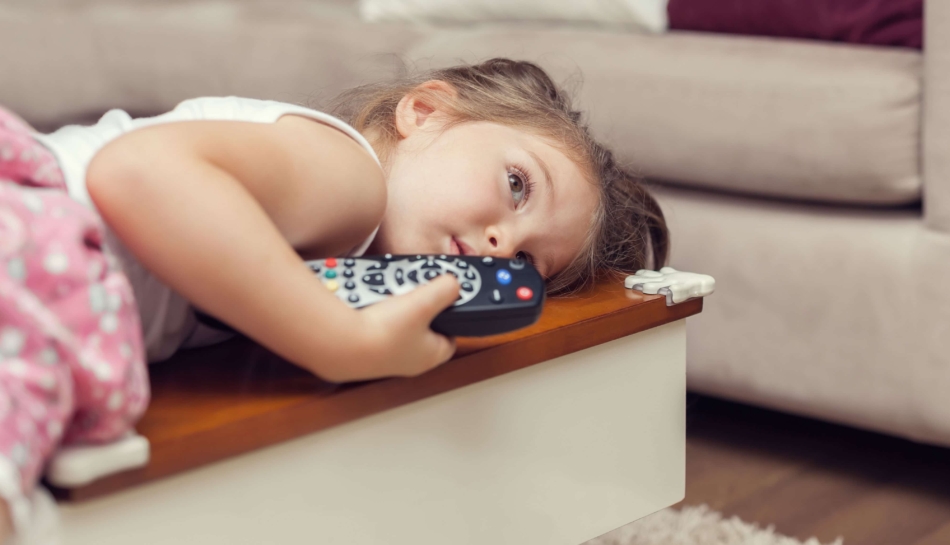 Bambina sdraiata sul divano con in mano il telecomando