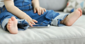 Bambino seduto sul divano che usa uno smartphone