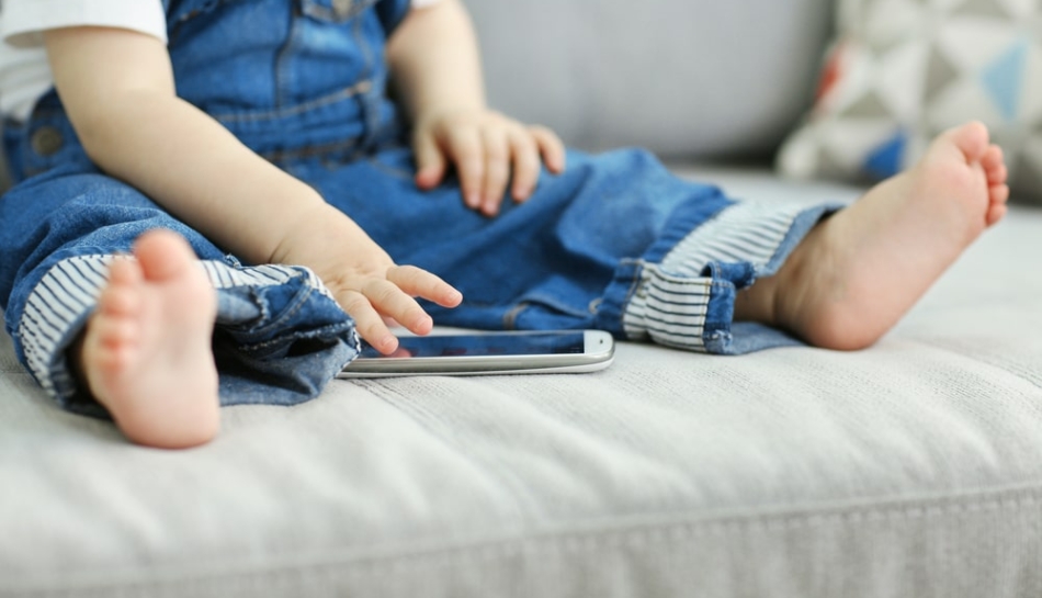 Bambino seduto sul divano che usa uno smartphone