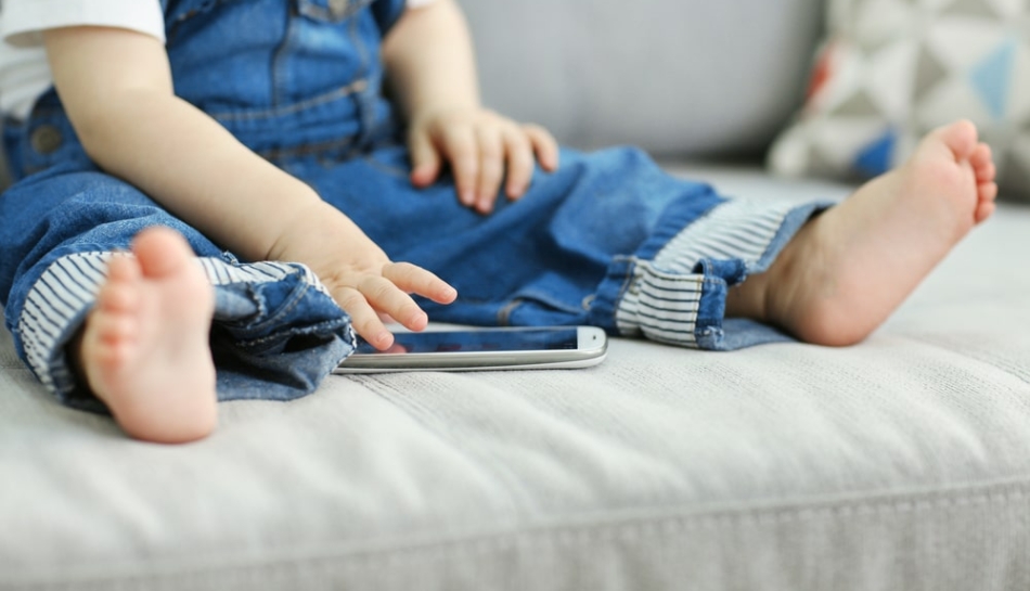 Bambino seduto sul divano che usa uno smartphone