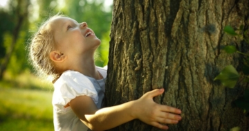 Bambina nella natura abbraccia un albero