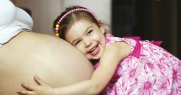 Bambina che abbraccia la pancia della mamma incinta