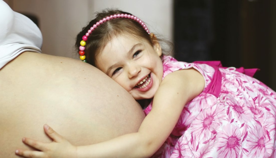 Bambina che abbraccia la pancia della mamma incinta