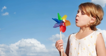 Bambina che soffia su una girandola colorata