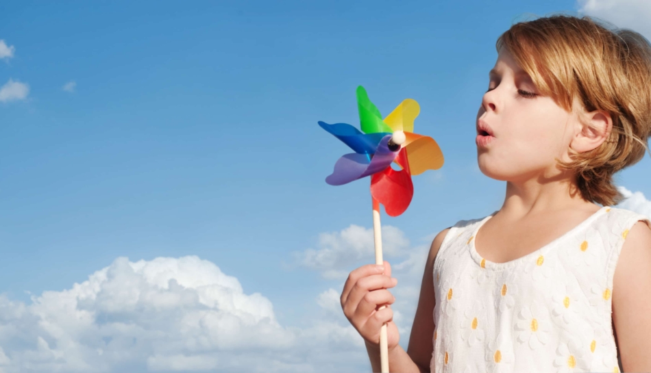 Bambina che soffia su una girandola colorata