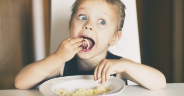 Bambina a tavola mangia la pasta con le mani