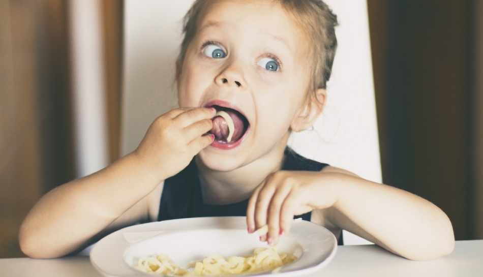 Bambina a tavola mangia la pasta con le mani