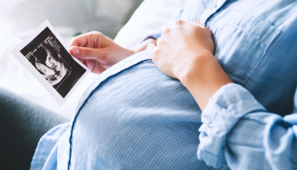 Primo piano della pancia di una donna in gravidanza che guarda un'ecografia
