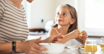 Bambina seduta a tavola a mangiare con la mamma