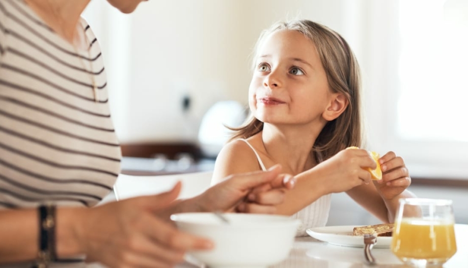 Bambina seduta a tavola a mangiare con la mamma