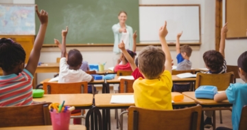 Children in a primary school classroom raising their hands