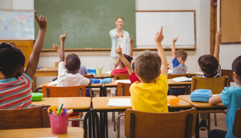 Bambini in una classe di scuola elementare che alzano la mano