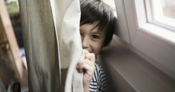 Bambino che per privacy si nasconde dietro a una tenda