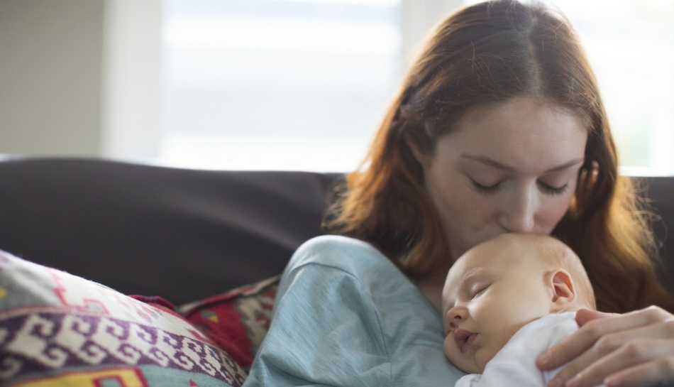 mamma che coccola il proprio neonato seduta su un divano