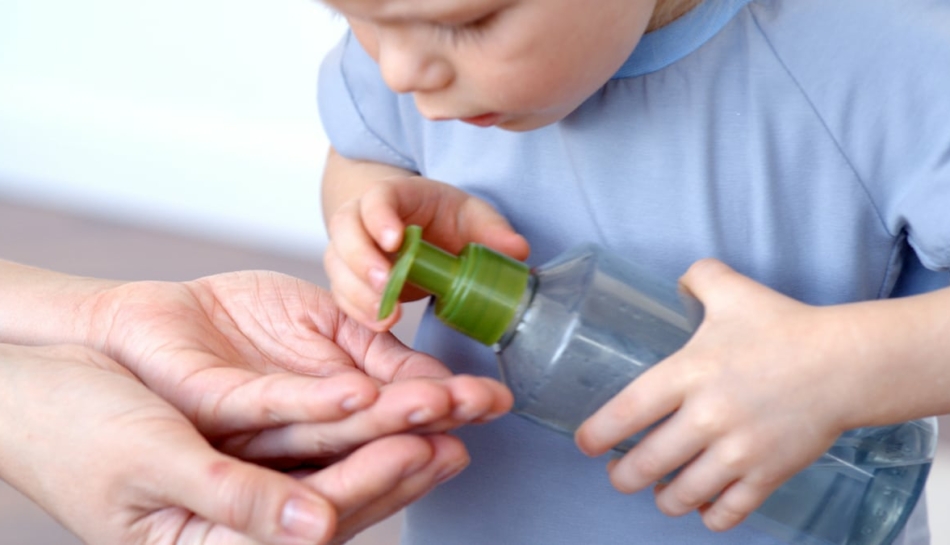 Primo piano di un bambino che versa del sapone sulle mani di un genitore