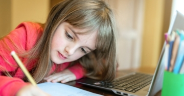 Bambina che scrive e segue al computer la didattica a distanza