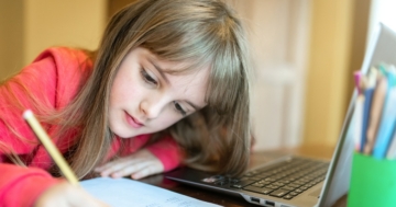 Little girl writing and watching distance learning on the computer