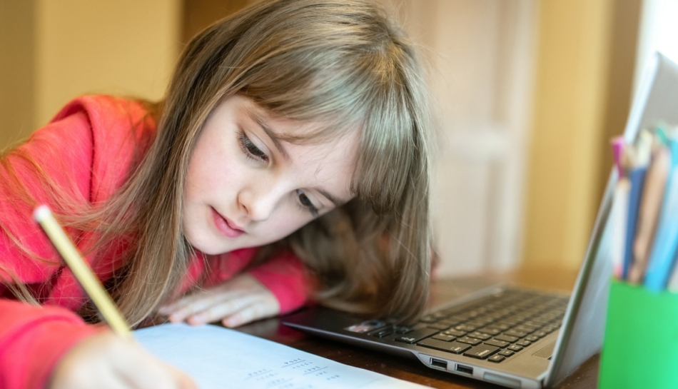 Bambina che scrive e segue al computer la didattica a distanza