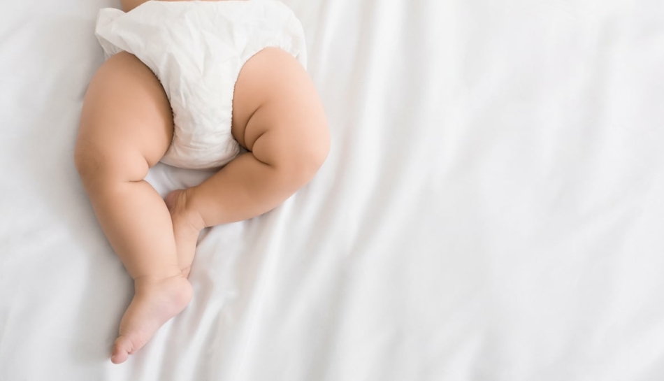 Gambe di un neonato sdraiato con indosso un pannolino