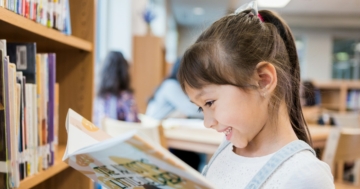 Bambina che legge un libro illustrato in biblioteca