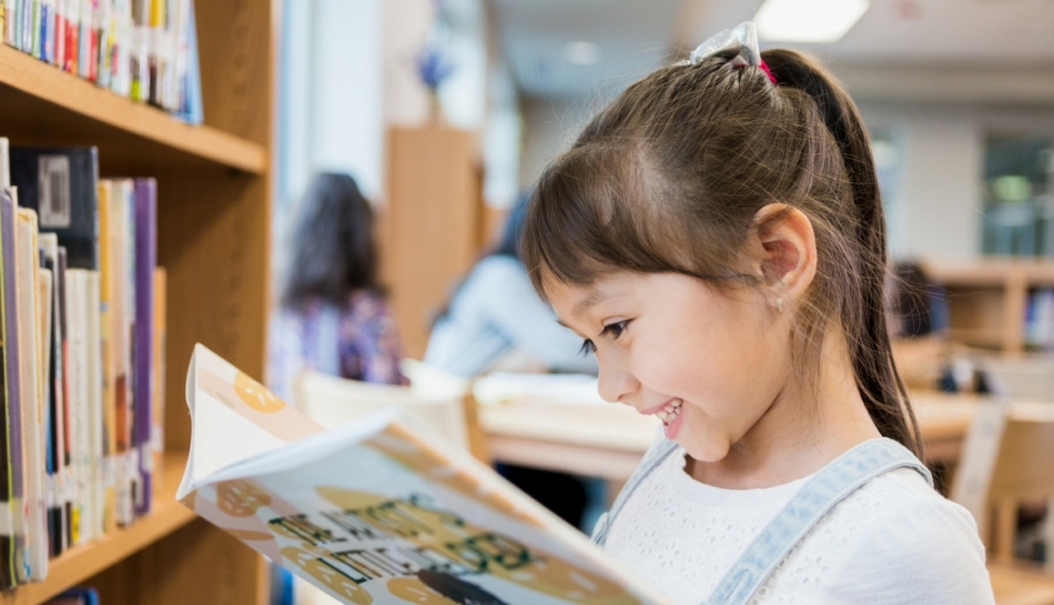 Bambina che legge un libro illustrato in biblioteca