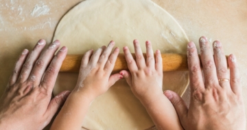 Bambino impasta in cucina con le mani assieme al genitore