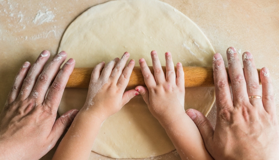 Bambino impasta in cucina con le mani assieme al genitore