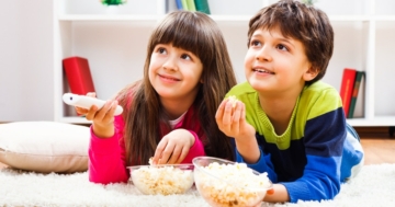 Bambini per terra che mangiano popcorn guardando la tv