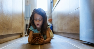 bambina sdraiata per terra che usa uno smartphone