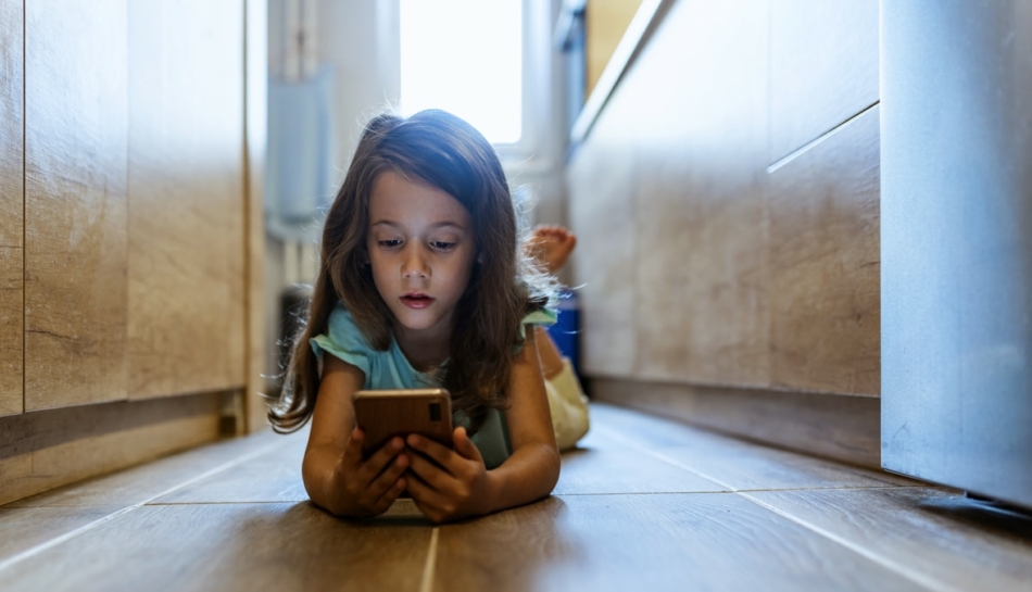 bambina sdraiata per terra che usa uno smartphone