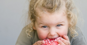 Primo piano di una bambina che addenta una ciambella