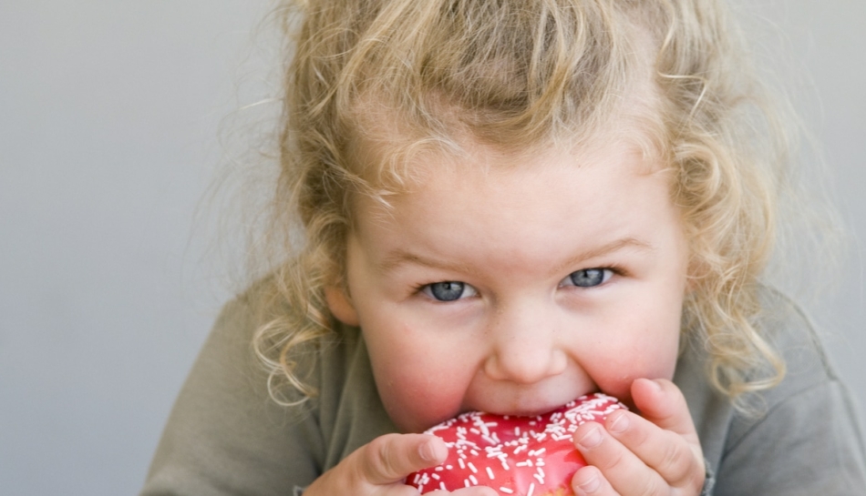 Primo piano di una bambina che addenta una ciambella
