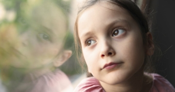 Bambina che guarda triste fuori dalla finestra