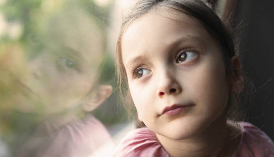 Bambina che guarda triste fuori dalla finestra