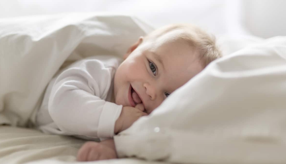Un bambino di circa 7 mesi disteso sul letto e sorridente