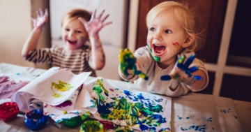 Two children are sitting at the table playing with tempera paints