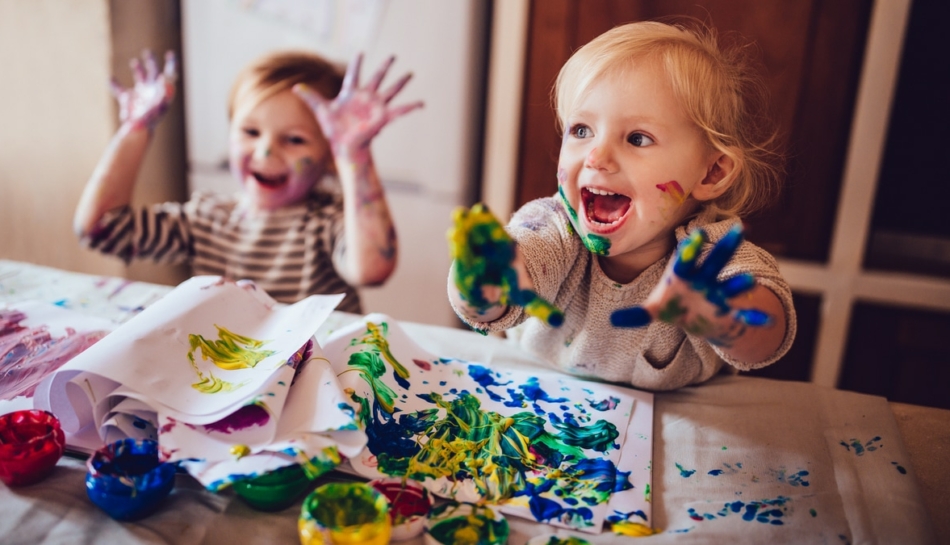 Due bambini seduti al tavolo che giocano con i colori a tempera