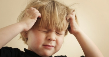 Primo piano di bambino che si tiene la testa tra le mani per il mal di testa