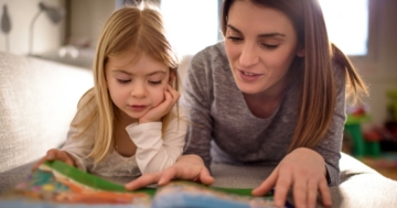 Bambina che legge un libro di fiabe in compagnia di uno dei suoi genitori, la mamma