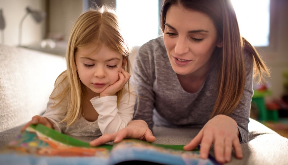 Bambina che legge un libro di fiabe in compagnia di uno dei suoi genitori, la mamma