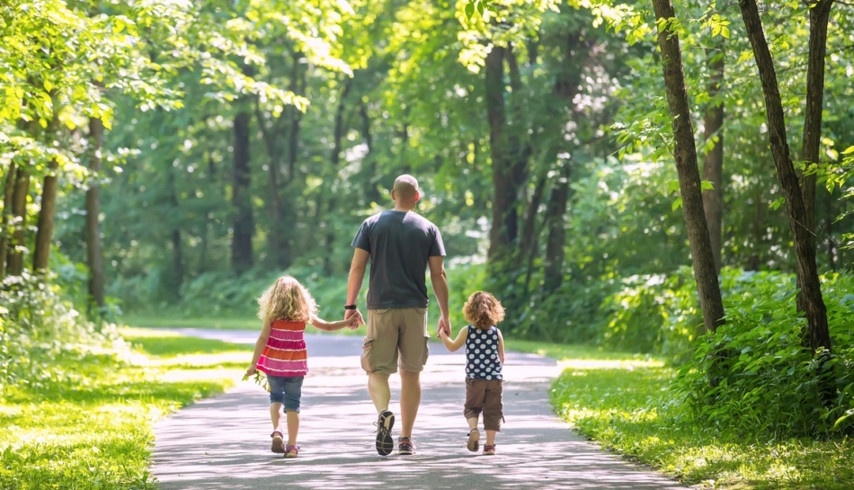 Un papà con i suoi bambini, di schiena, camminano in un ambiente naturale, tutelando la propria salute